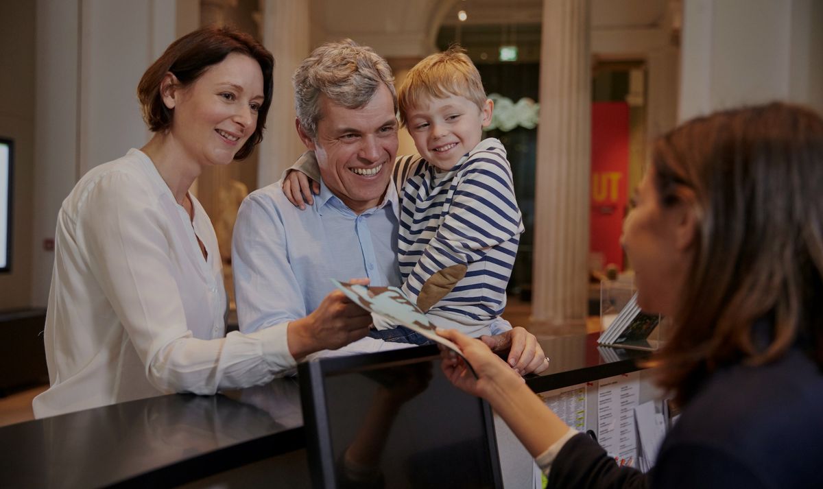 Family receiving tickets from a receptionist at a counter in a museum.