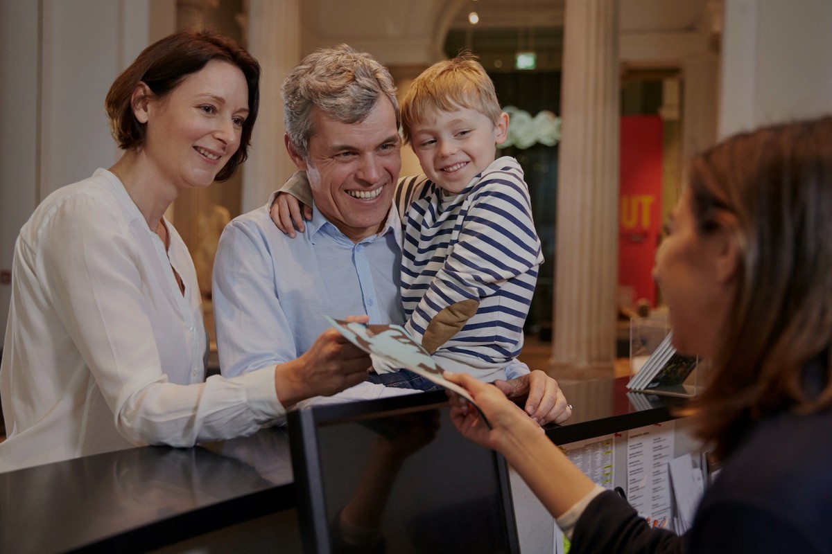 Family receiving tickets from a receptionist at a counter in a museum.