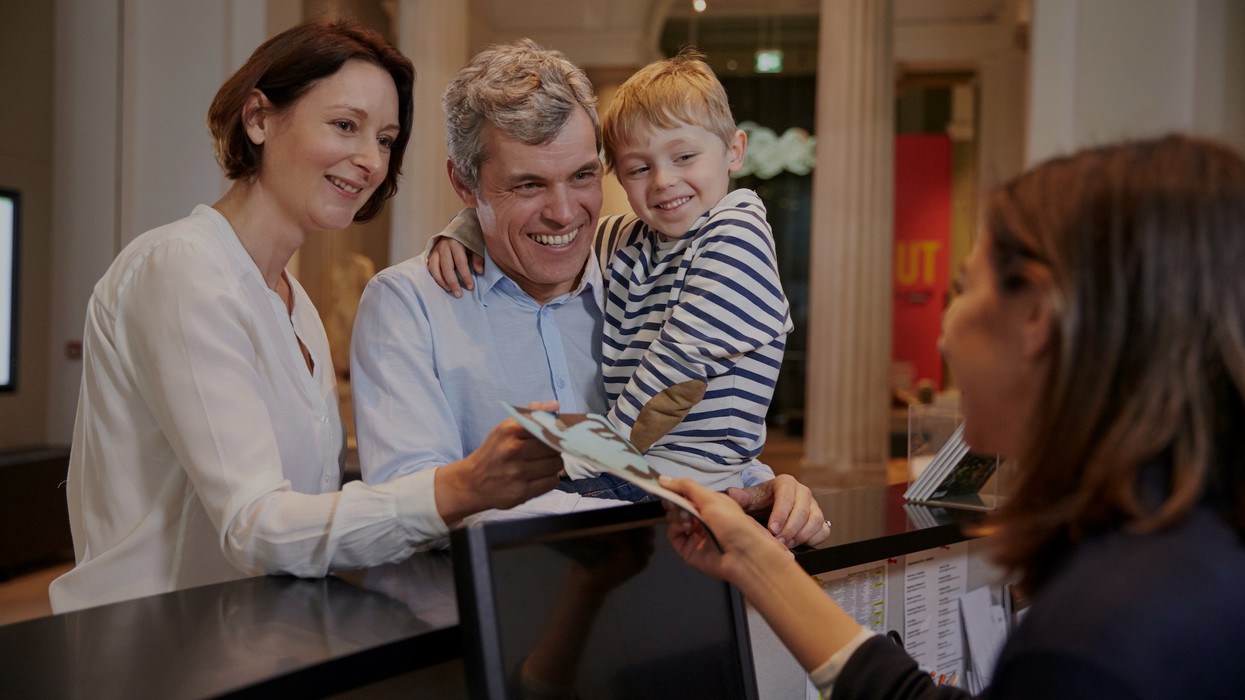 Family receiving tickets from a receptionist at a counter in a museum.