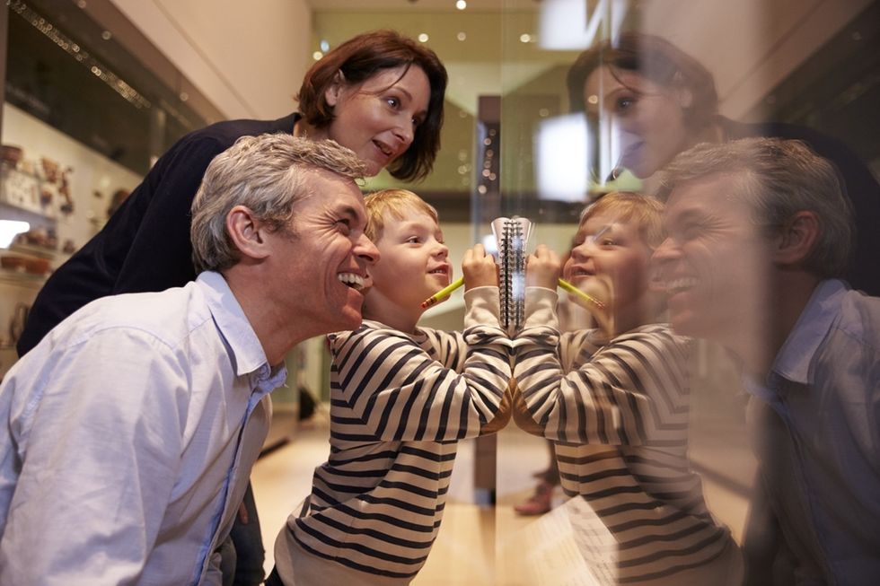 Family smiling and watching a young boy drawing on a museum display glass.