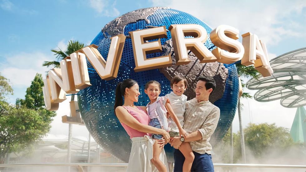 Family smiling in front of Universal globe sculpture, with blue sky and trees behind at Universal Studios Singapore