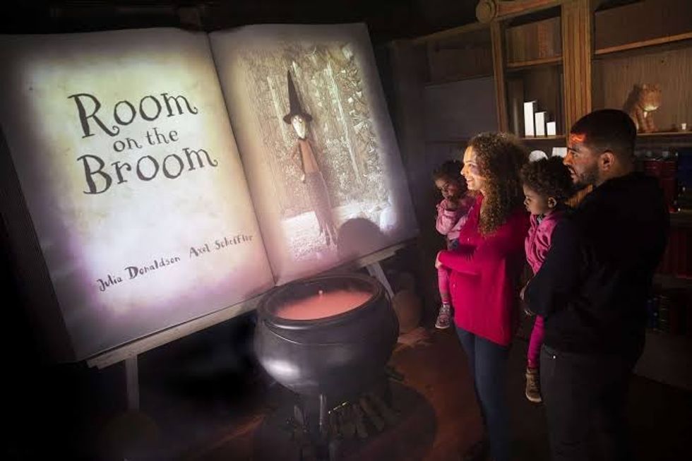Family viewing "Room on the Broom" book projection next to a large black cauldron.