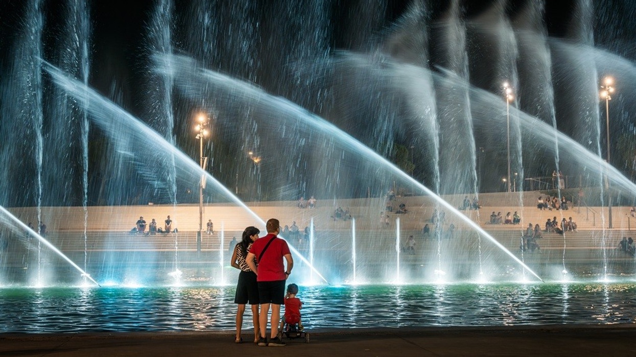 Family watching illuminated fountains at night with seated spectators in the background.