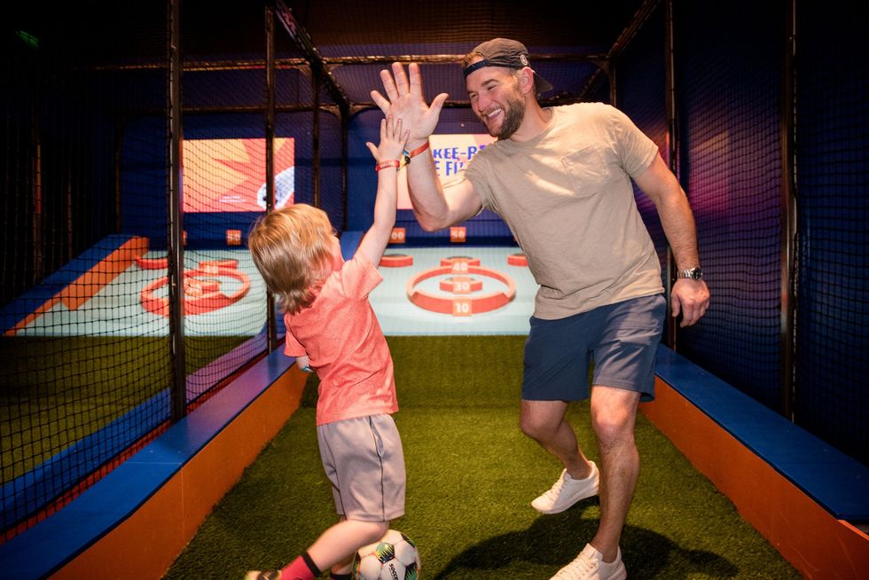 Father and son high-five in an indoor sports game area, celebrating a fun moment.
