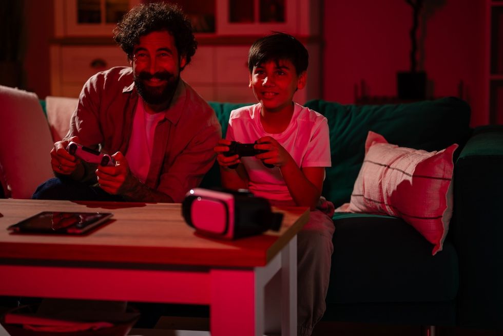Father and son playing video games on a couch, lit by a red light.