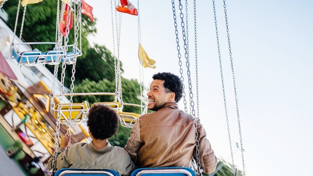 Father And Son Riding Swing Set At Fun Fair