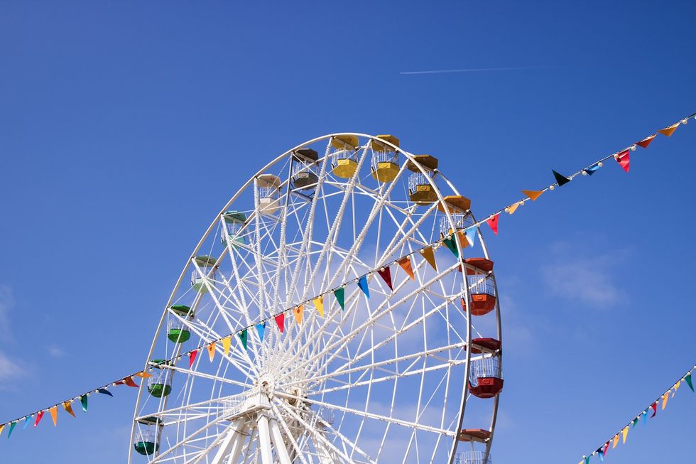 Ferris wheel against blue sky with colorful flags and a distant jet trail at Dreamland Margate