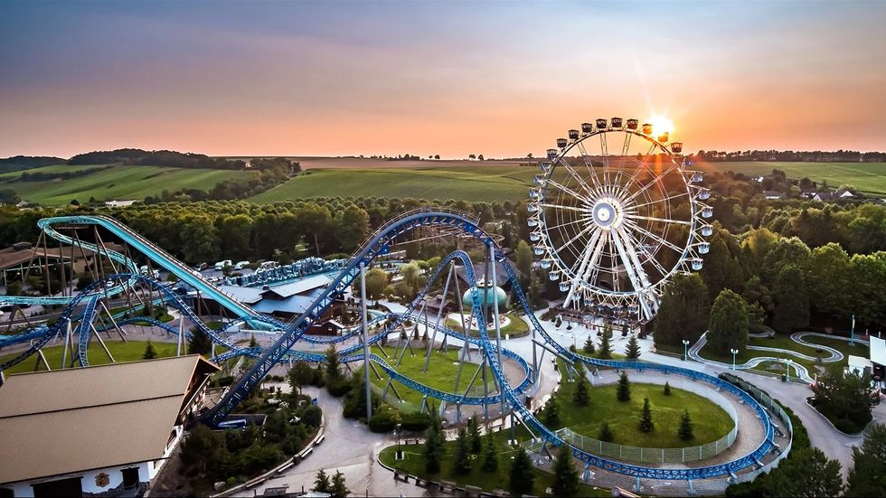 Ferris wheel and roller coaster at an amusement park called Nigloland during sunset with scenic countryside.