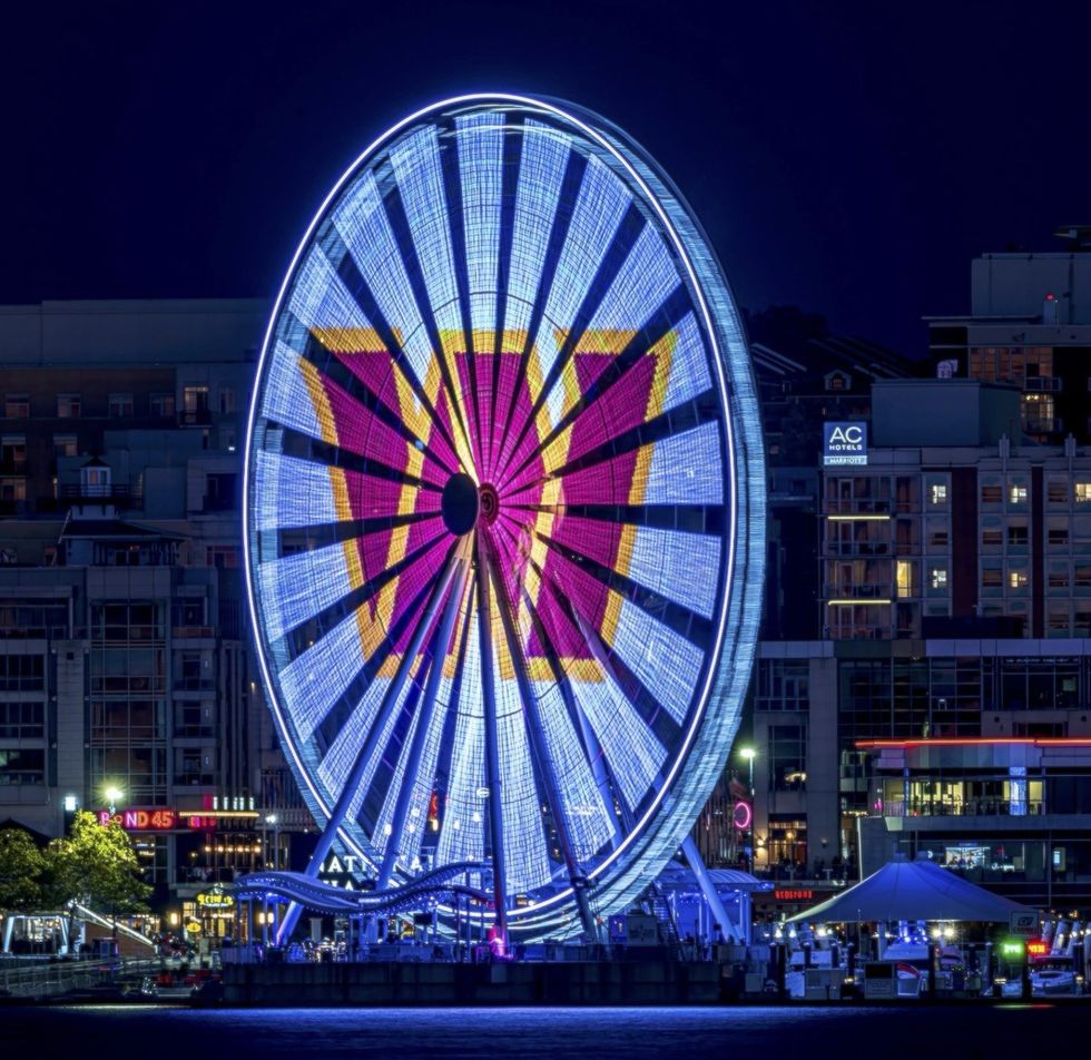 Ferris wheel lit with colorful lights against a city backdrop at night.