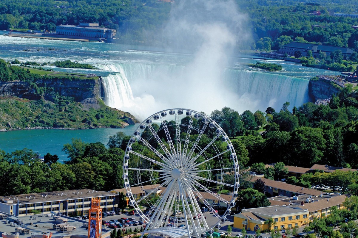 Ferris wheel overlooking Niagara Falls, surrounded by lush greenery and buildings.