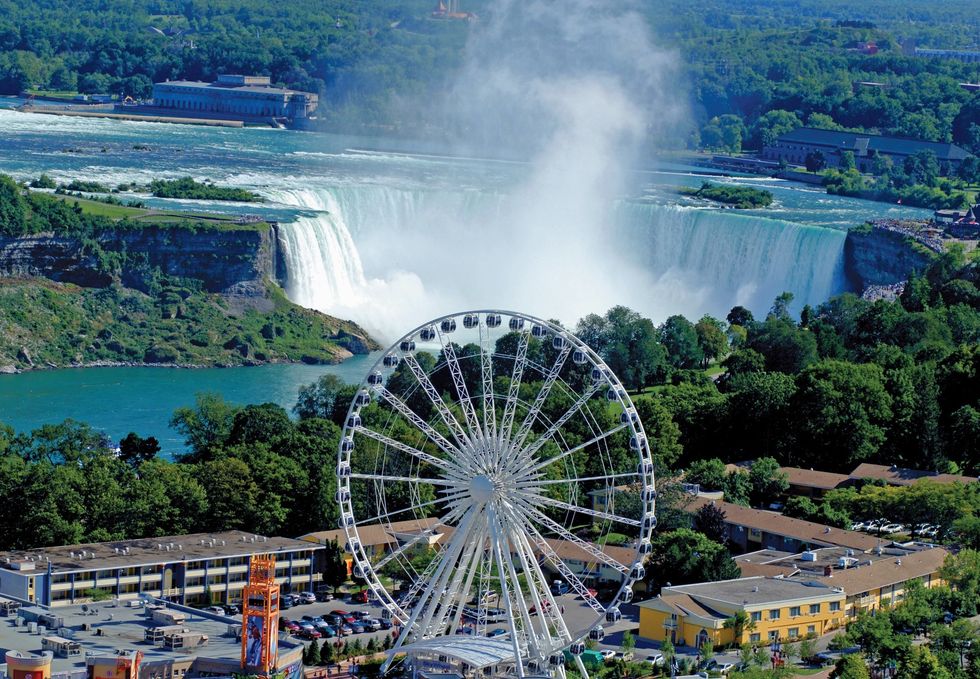 Ferris wheel overlooking Niagara Falls, surrounded by lush greenery and buildings.