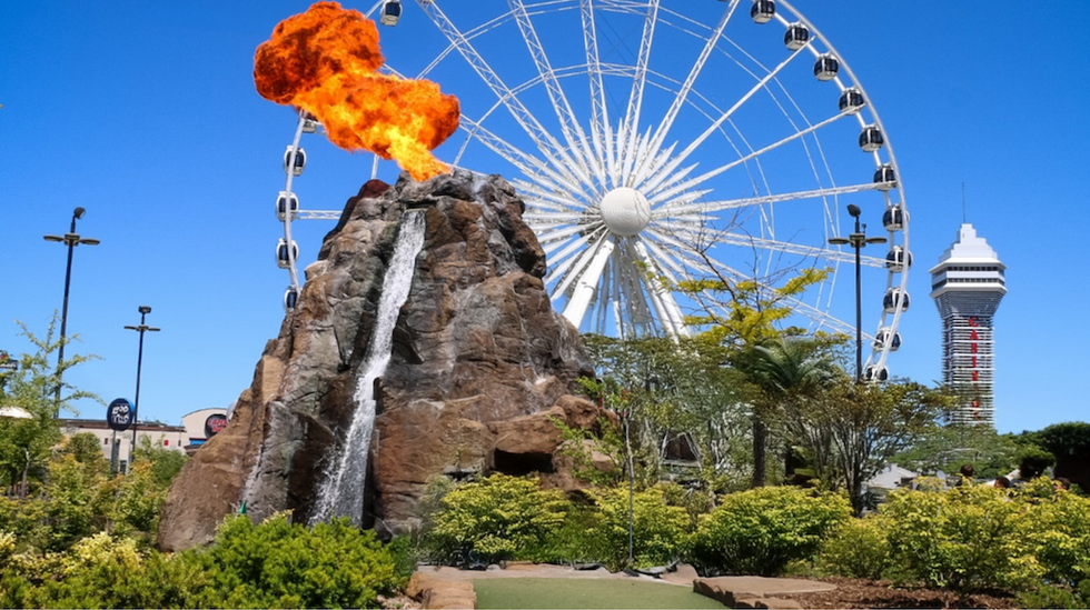 Ferris wheel, tower, and erupting volcano fountain in a park setting.