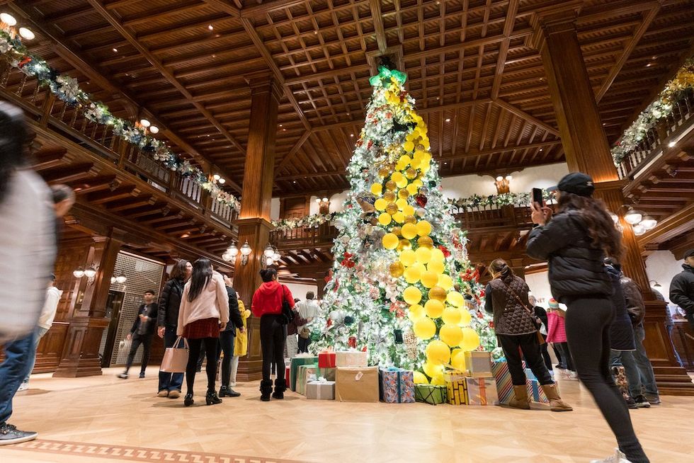 Festive hotel lobby with large decorated Christmas tree and people taking photos.