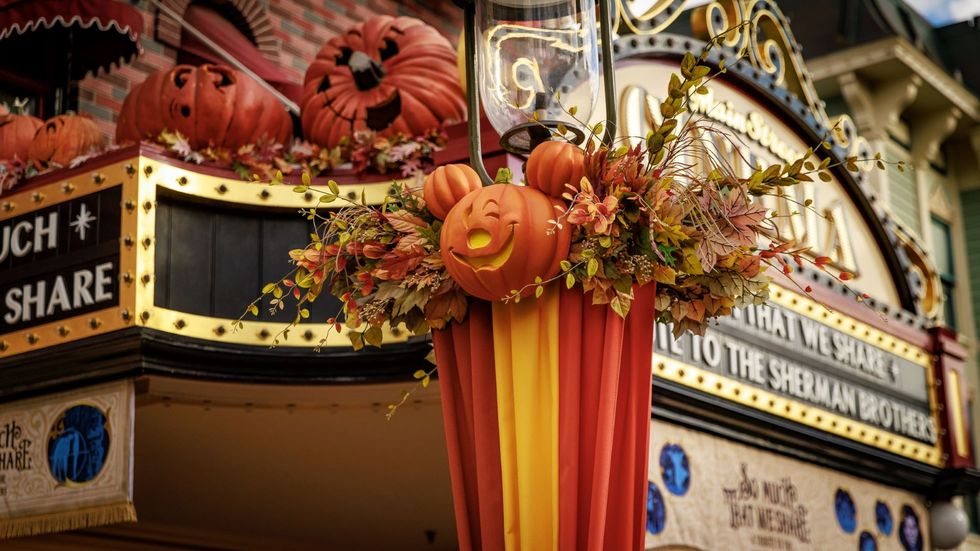 Festive pumpkin decorations on a building at Disneyland with autumn leaves and banners.