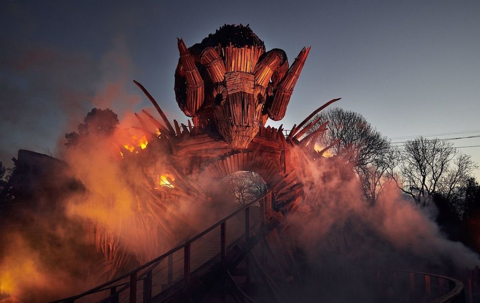 Fiery wooden sculpture with horns, surrounded by smoke at dusk.