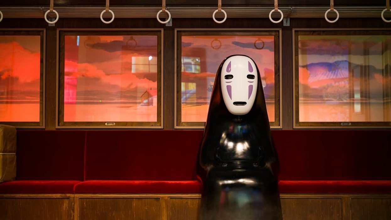 Figure with white mask sits on red train seat against sunset backdrop.