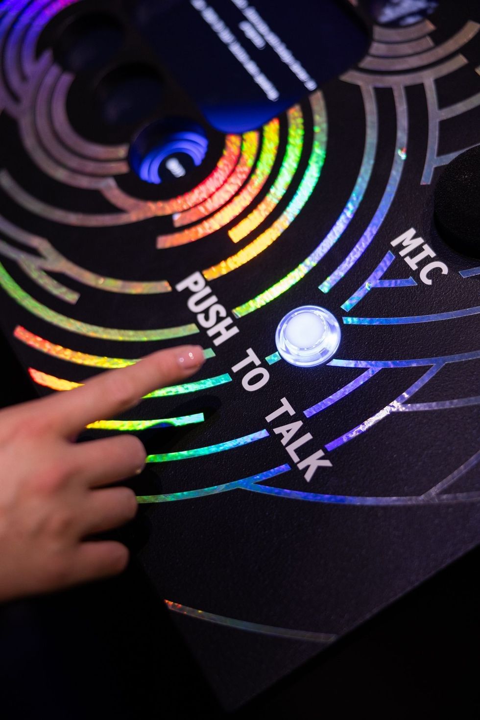 Finger pressing "Push to Talk" button on a colorful, circular patterned surface.