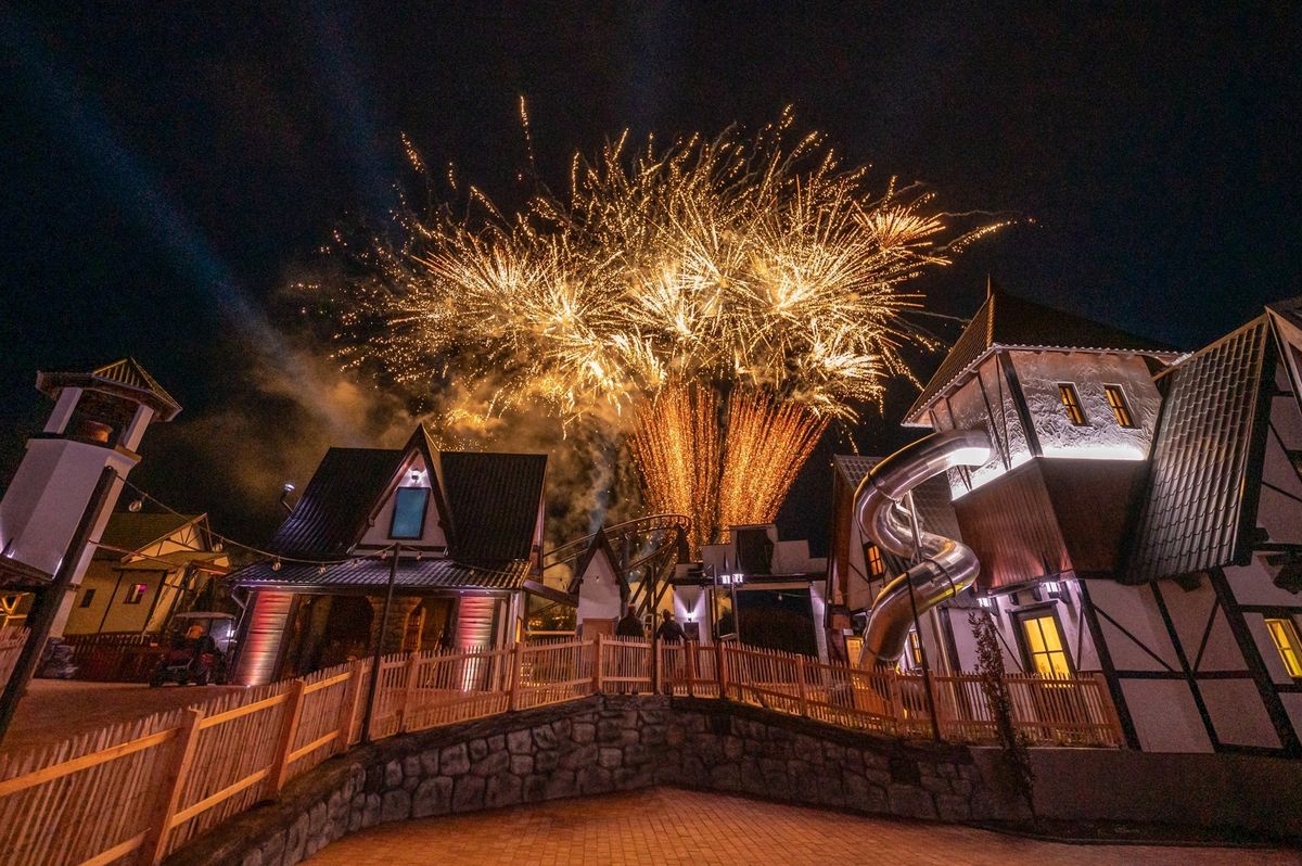 Fireworks illuminate a village scene at night with charming, rustic cottages and slides.
