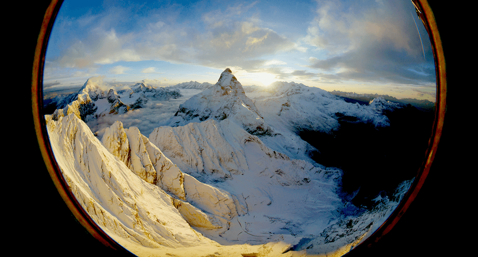 Fish-eye view of snowy mountains at sunrise, captured through a circular window.