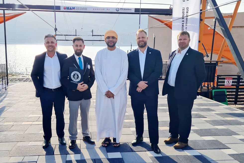 Five men in suits standing next to OAC Zipline one holding a Guinness World Records plaque.