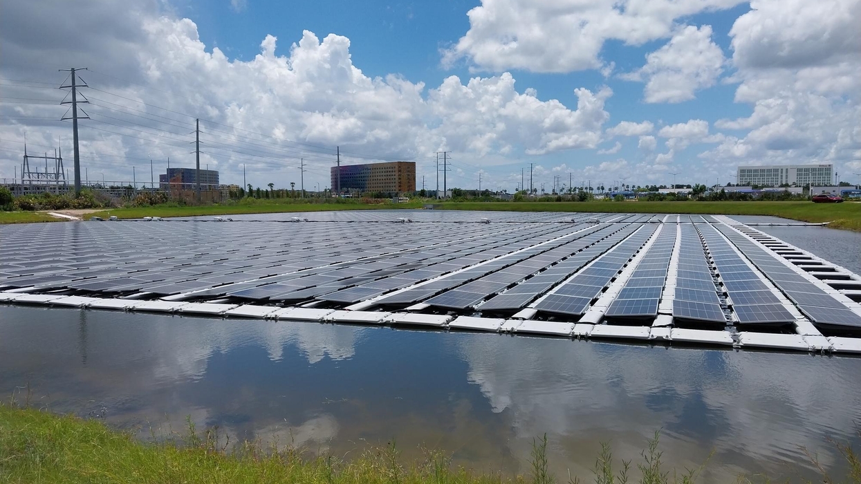 Floating solar panels on a pond under a partly cloudy sky, with distant buildings at Universal Epic Universe