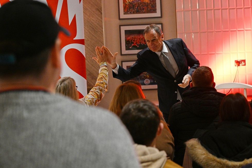 Football legend Phil Thompson high-fives seated woman in a crowd, red lighting and framed photos in background.