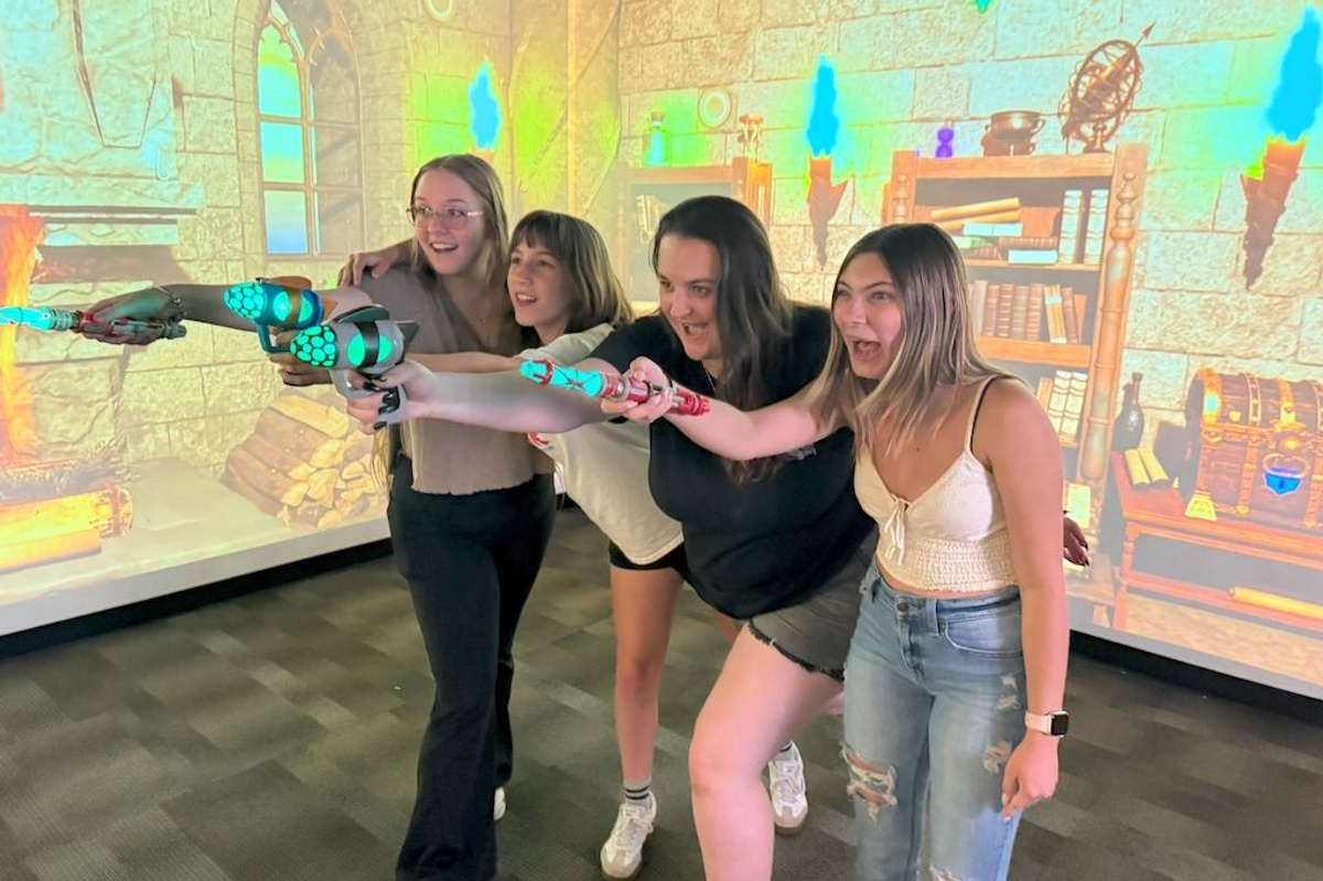 Four excited people holding toy guns in a medieval-themed virtual room.