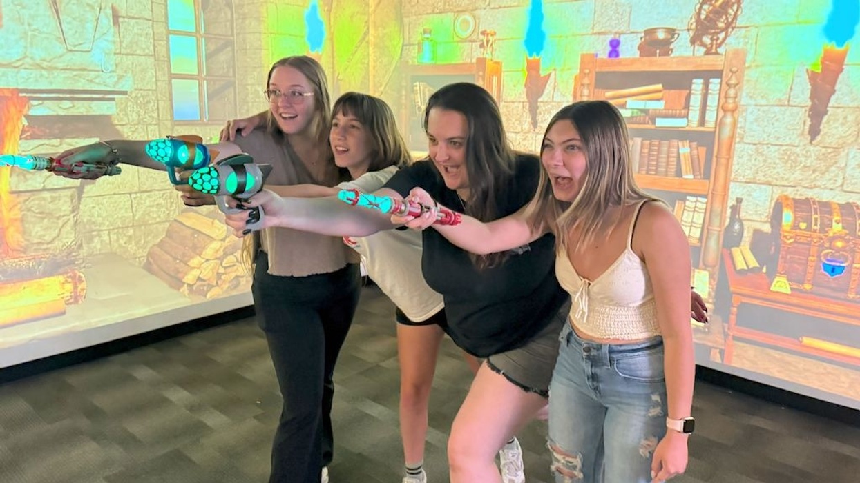 Four excited people holding toy guns in a medieval-themed virtual room.