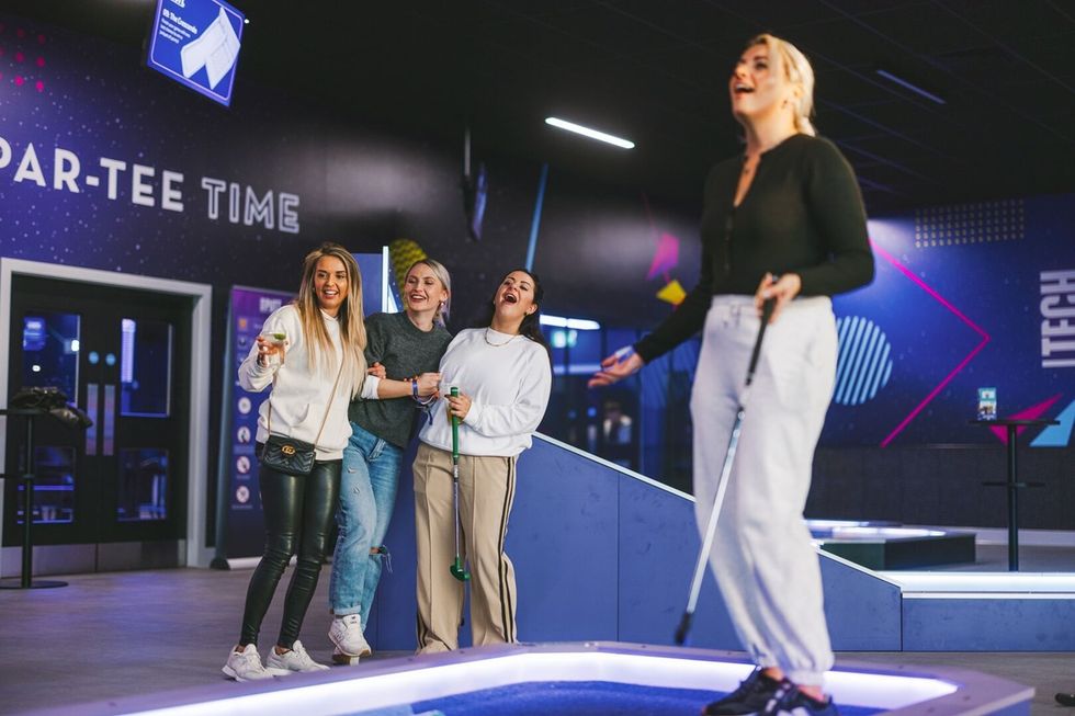 Four friends enjoying mini golf from 360Golf indoors, with "Par-Tee Time" sign in the background.