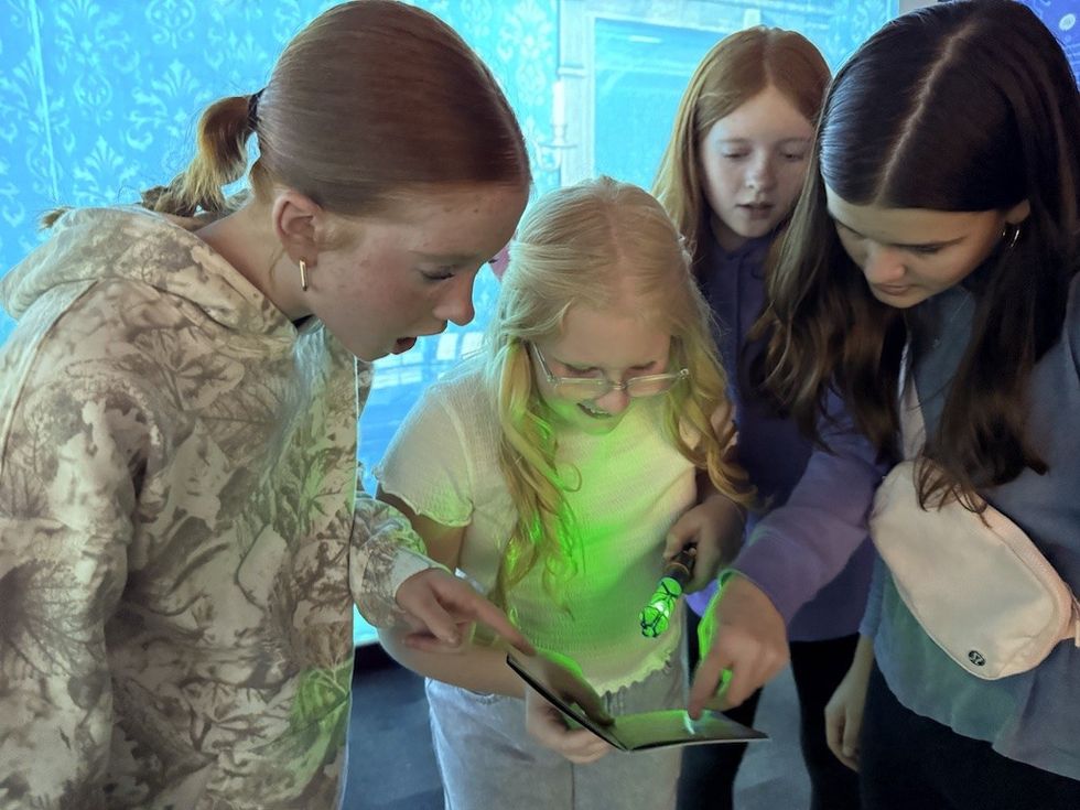 Four girls examining a glowing book with curiosity.