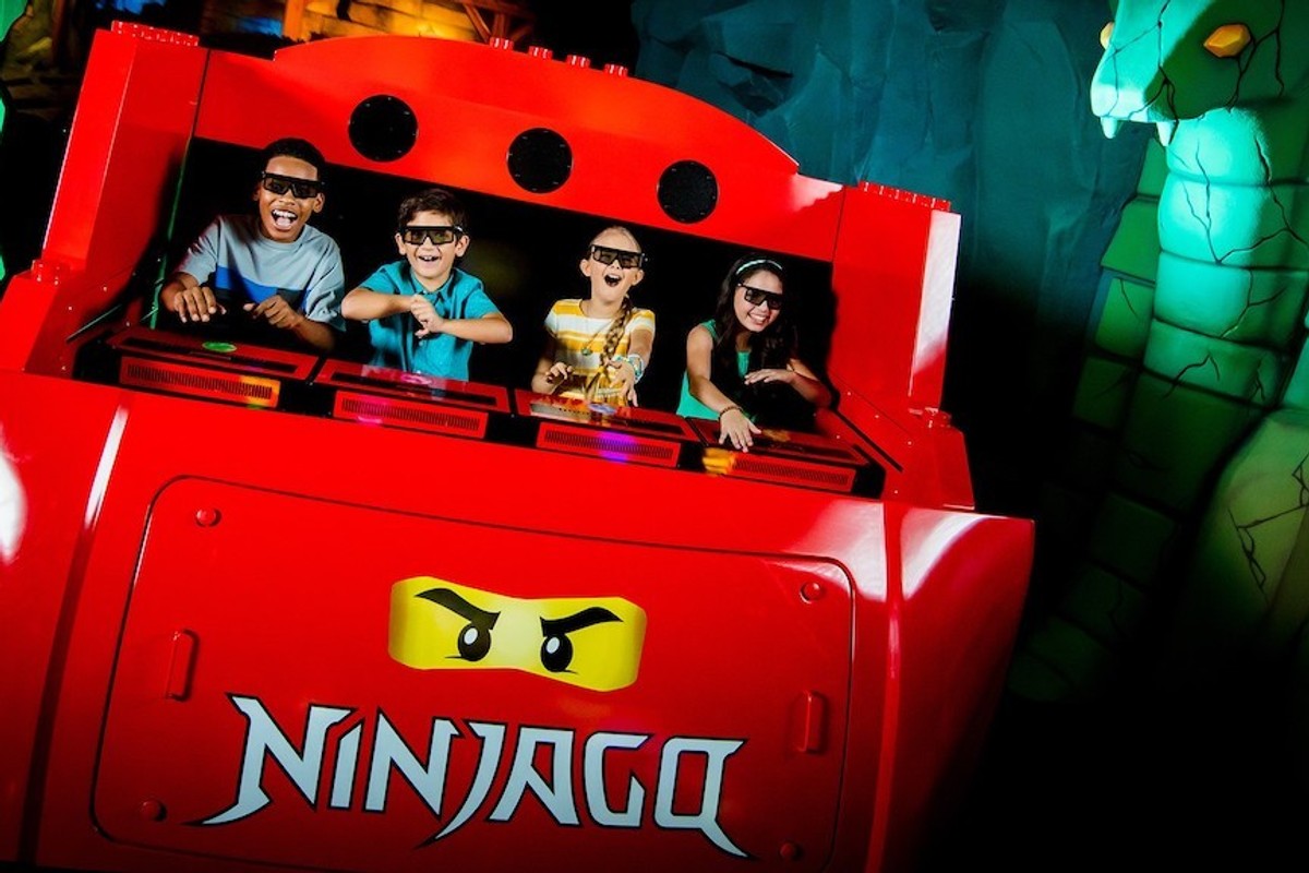 Four kids enjoy a 3D Ninjago ride at an amusement park, wearing 3D glasses.