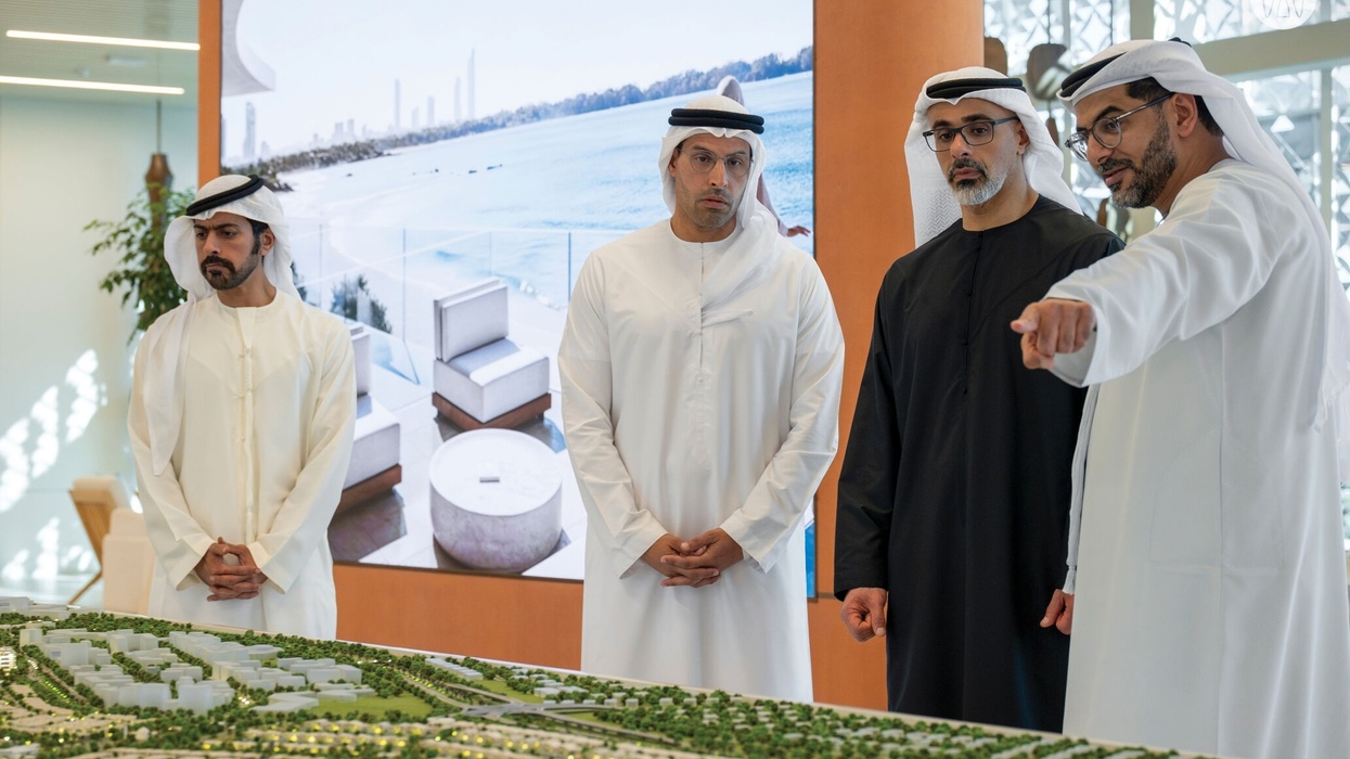 Four men in traditional attire discuss an architectural model of Marsa Al Saadiyat