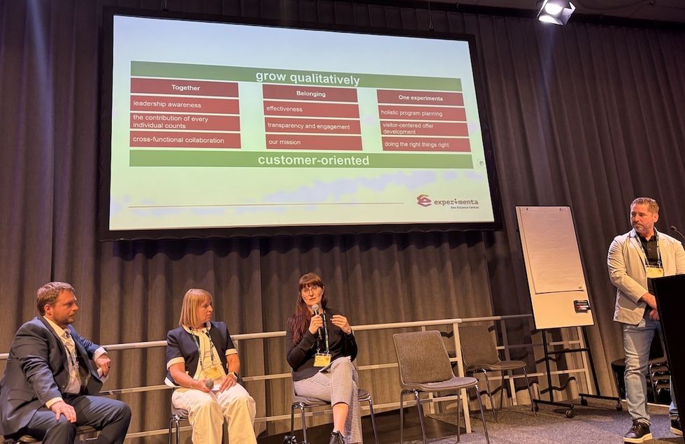 Four people discuss in front of a projector screen showing organizational values.