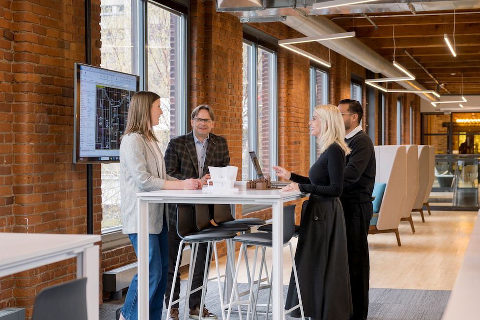 Four people discussing at a high table in a modern office with brick walls.