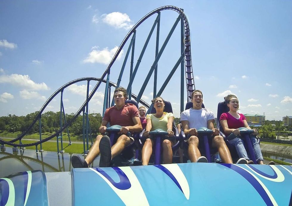 Four people excitedly riding a roller coaster under a bright blue sky at SeaWorld Orlando