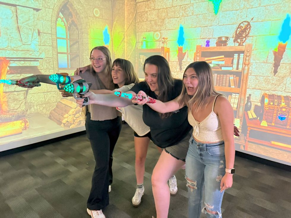 Four people having fun with VR wands in a medieval-themed room.