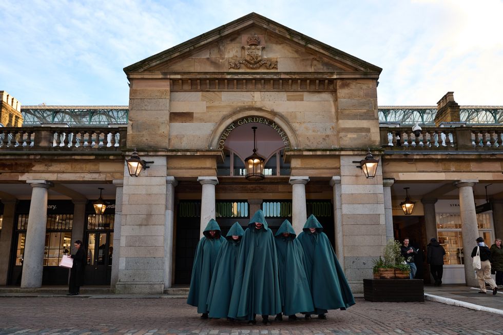 Four people in teal cloaks outside Covent Garden Market.