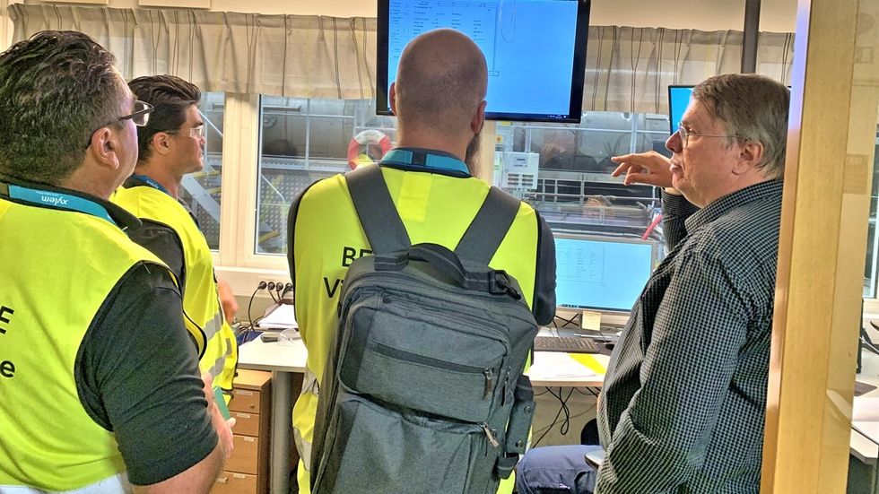 Four people in vests observe a ozone system monitor in an office setting.