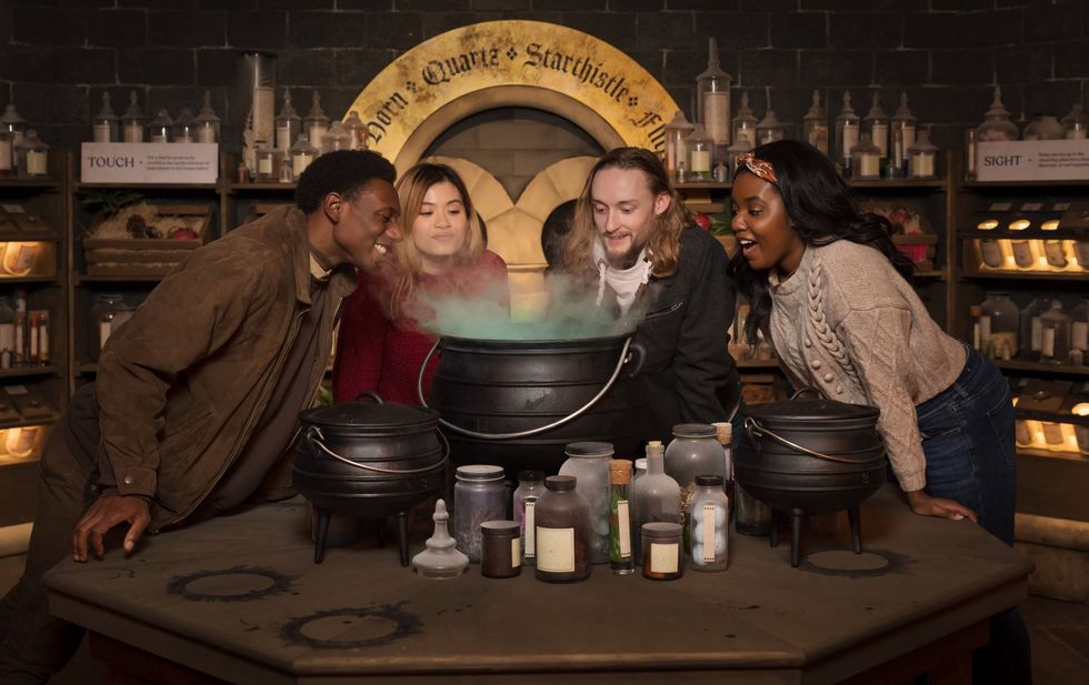 Four people intrigued by a steaming cauldron in a potion-filled room at Harry Potter: Magic at Play