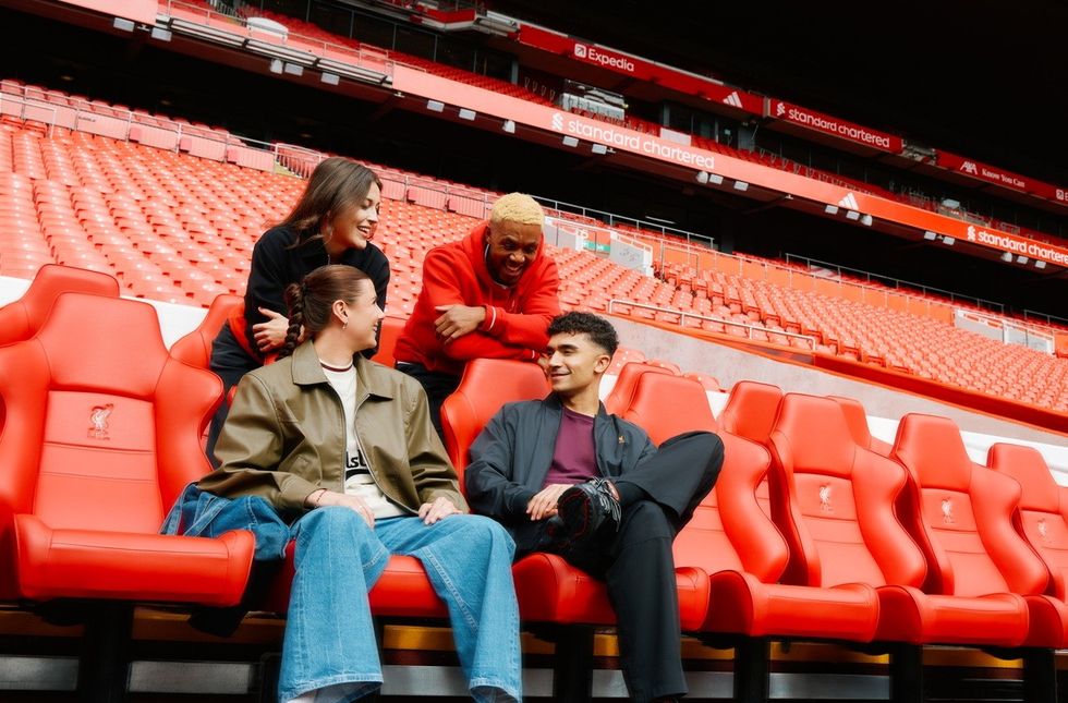 Four people laughing on red stadium seats, with empty stands in the background.