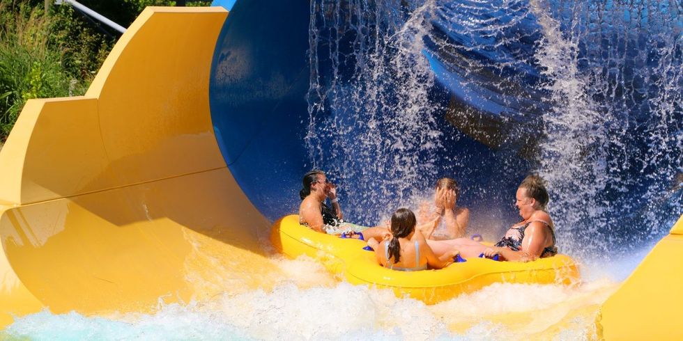 Four people on a yellow raft ride a water slide, water splashing around them at Six Flags White Water Atlanta