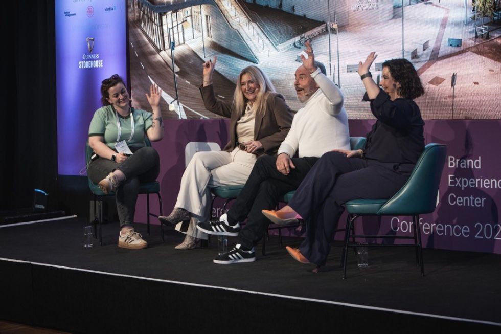 Four people on stage, smiling and raising hands during a Brand Experience Center Conference panel discussion