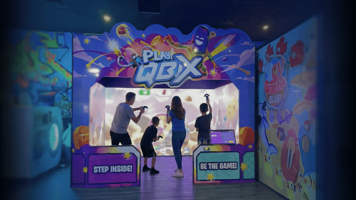 Four people playing an interactive arcade game, "Play QBIX," with colorful graphics.