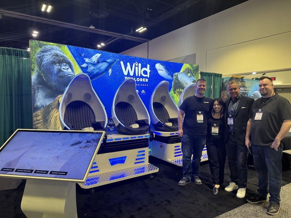Four people pose by virtual reality pods at a "Wild Explorer" exhibit with nature images.
