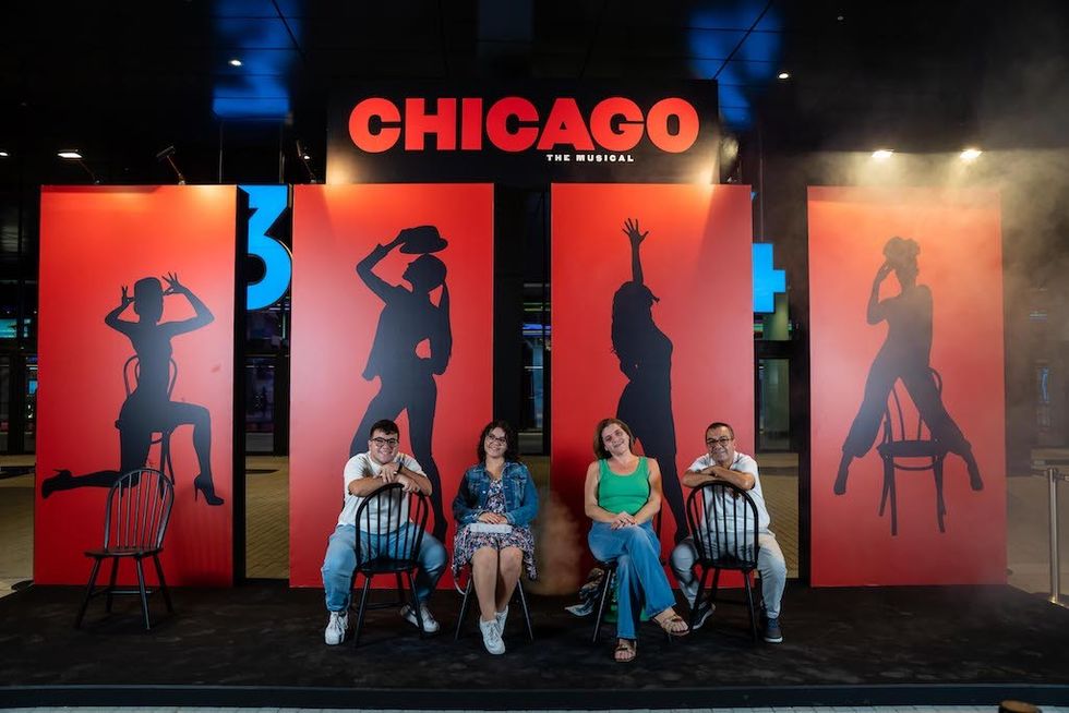 Four people pose in front of "Chicago" musical silhouettes and signage.