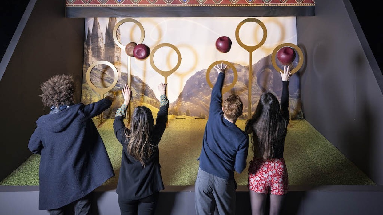 Four people reaching for Quidditch hoops on a themed display with red balls.