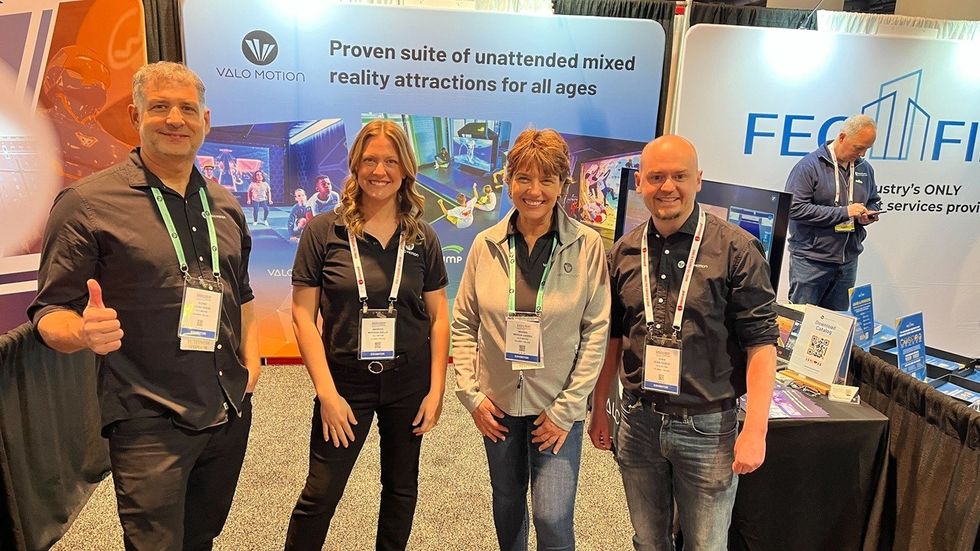 Four people smiling at a trade show booth for Valo Motion with promotional displays.
