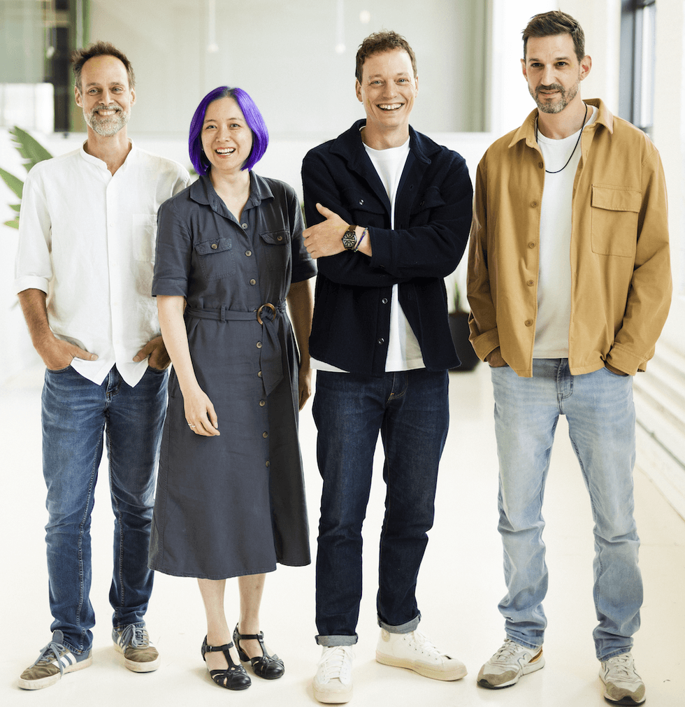 Four people smiling together, standing in a bright room.