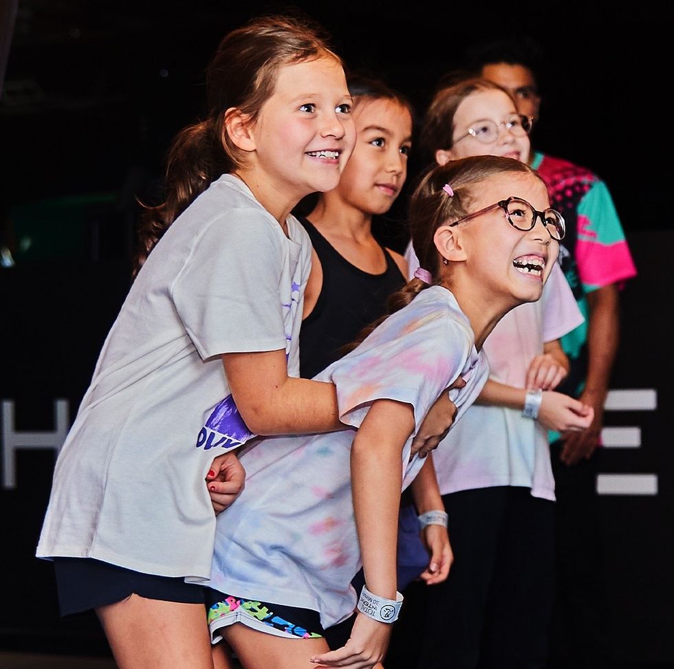 Four smiling kids in casual clothing, enjoying a fun moment together indoors.