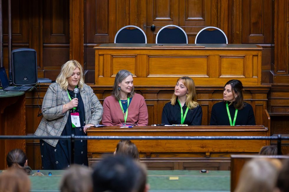 Four women panelists in a wooden courtroom setting, one speaking into a microphone.